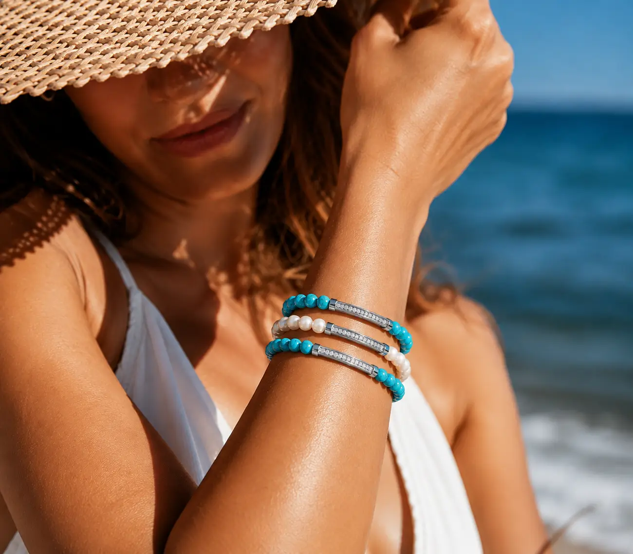 Bracelets Pearl turquoise et nacre portés à la plage, chapeau de paille et mer en fond